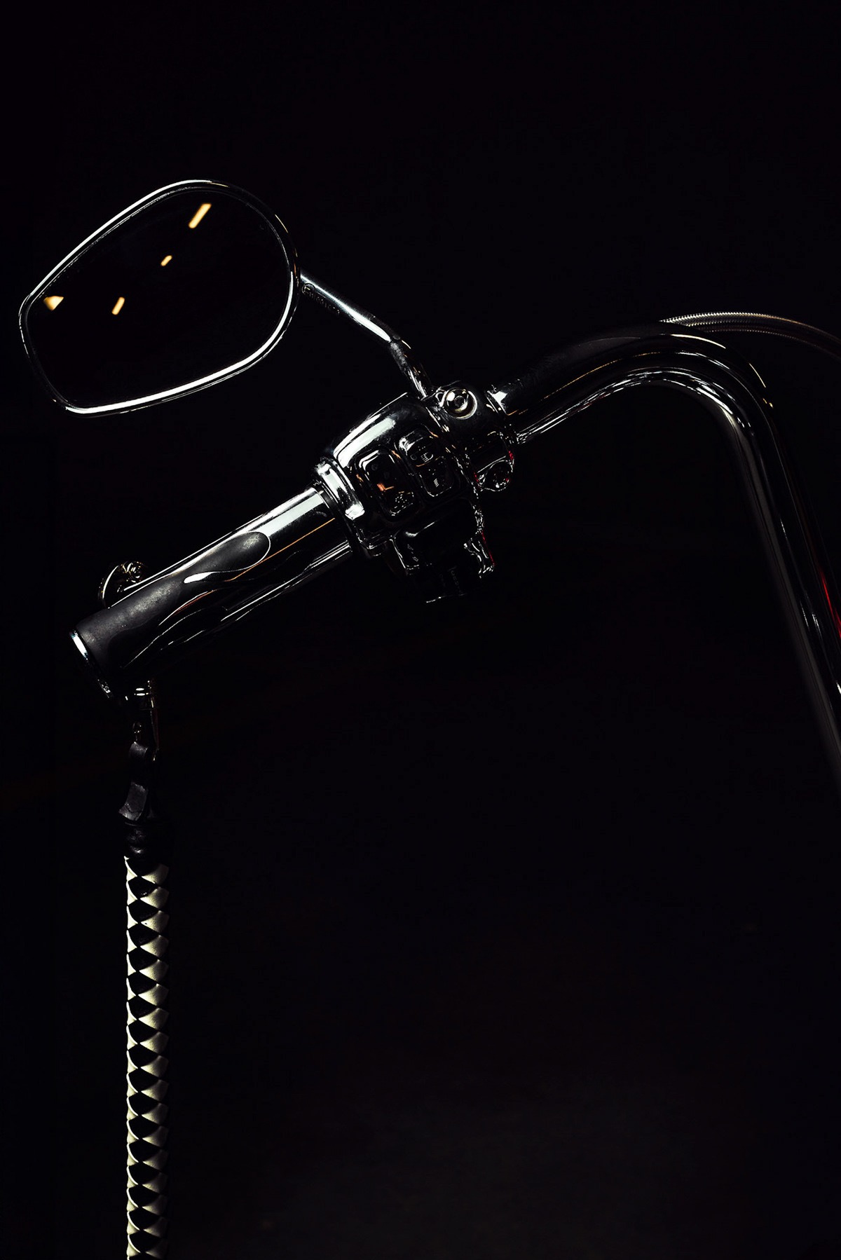 Chromowana kierownica motocykla typu chopper z lusterkiem i czarno-białym frędzlem, sfotografowana w Krakowie na ciemnym tle.