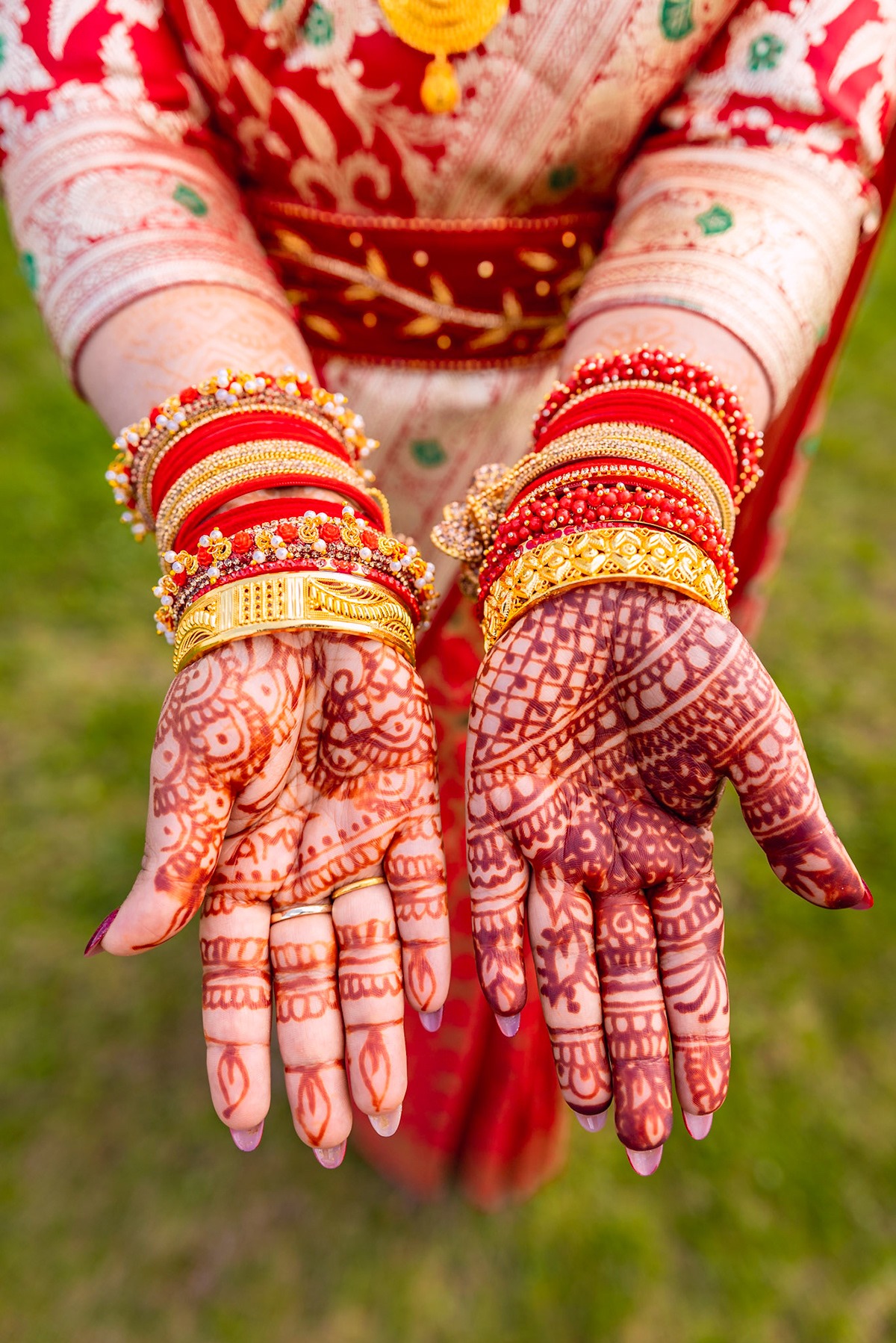 Dłonie kobiety zdobione henną i licznymi, kolorowymi bransoletami, prezentowane na tle czerwonej, wzorzystej sukni.