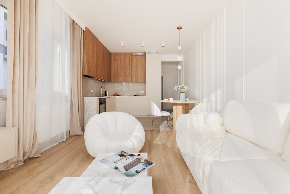 Jasne wnętrze mieszkania z drewnianą zabudową kuchenną, marmurowym stolikiem kawowym i okrągłym fotelem, oświetlone naturalnym światłem wpadającym przez okno z beżowymi zasłonami.