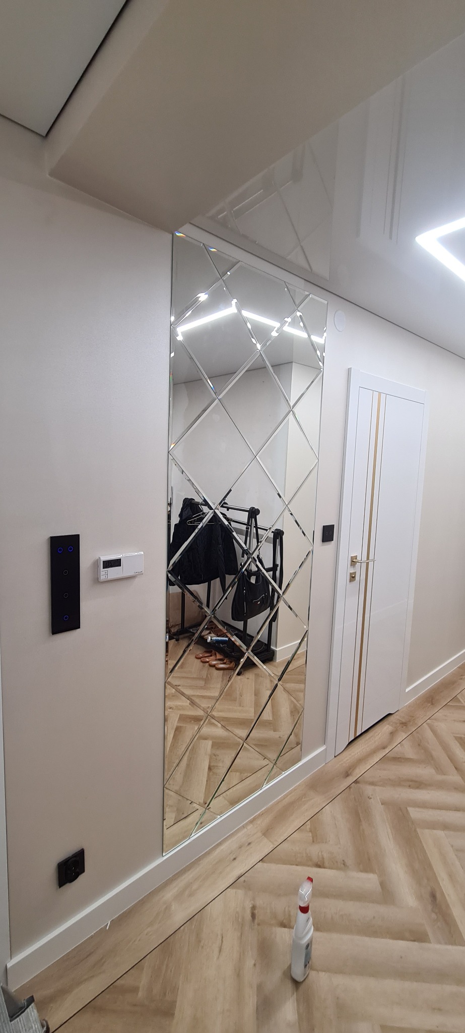 Dekoracyjne lustro z rombów w przedpokoju w Głogowie Małopolskim. Widoczne odbicie wieszaka na ubrania i podłogi. Nowoczesne wykończenie wnętrza.