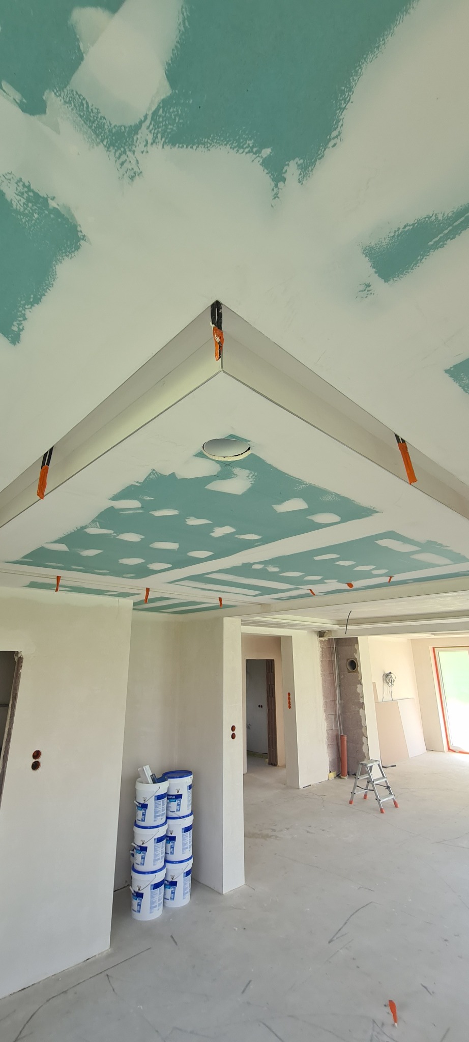 Sufit podwieszany z płyt gipsowo-kartonowych w trakcie montażu, widoczne profile, szpachlowane łączenia, taśma wzmacniająca. W tle puste pomieszczenie w stanie deweloperskim.