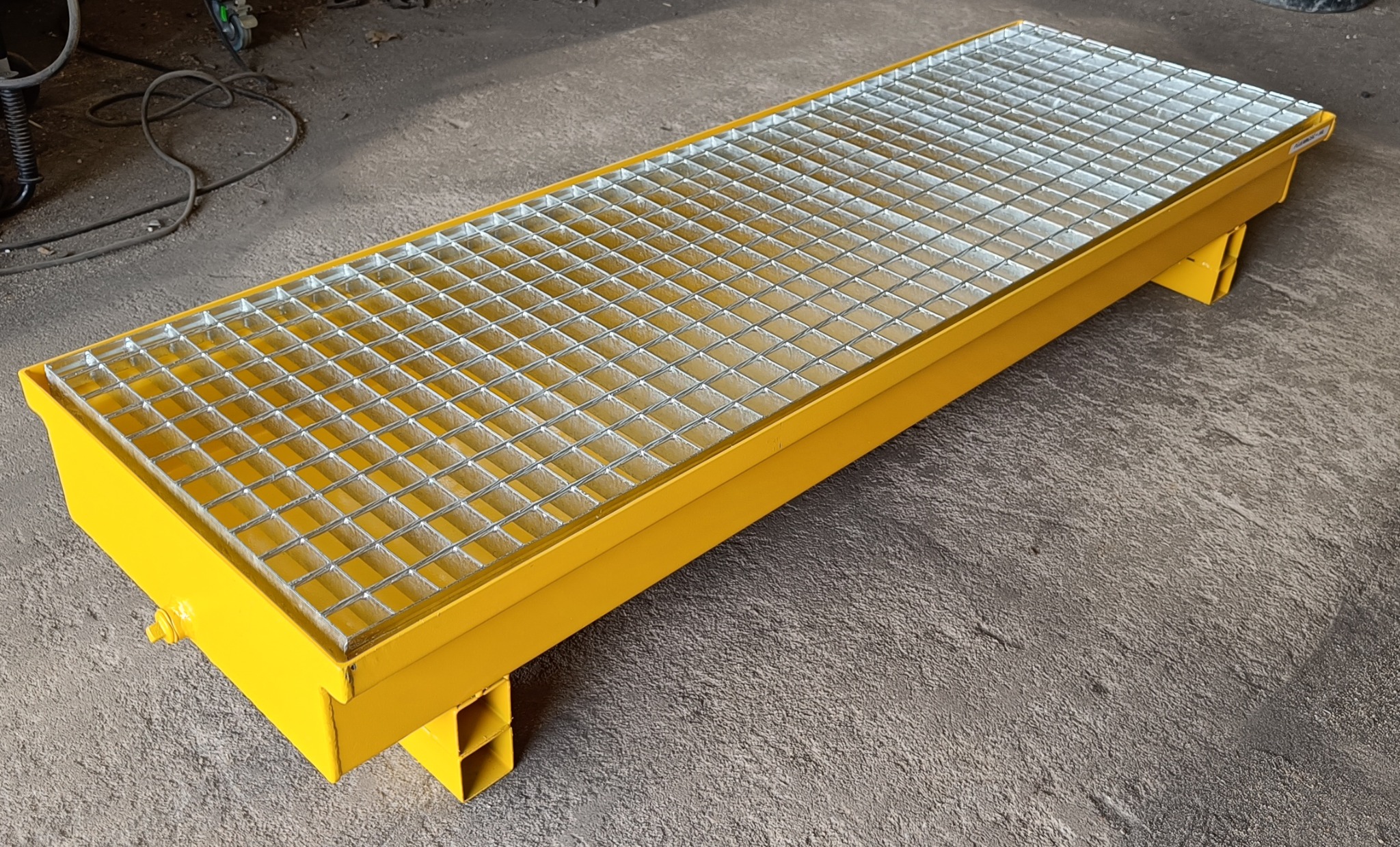 Żółta, prostokątna platforma z metalową kratą, spawana konstrukcja stalowa na podłożu betonowym.