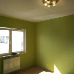 Pomalowane na zielono puste pomieszczenie z parkietem, grzejnikiem pod oknem i nowoczesną lampą sufitową.