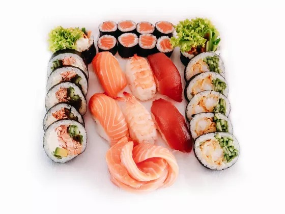 Zestaw sushi z łososiem, tuńczykiem, krewetkami i warzywami, ułożony symetrycznie na białym tle, z wyraźnie widocznymi rolkami maki i nigiri.