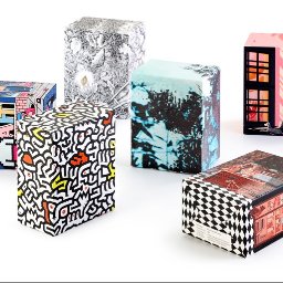 ANS Group Spółka z ograniczona odpowidzialnością - Sześć prostopadłościennych pudełek z różnorodnymi, artystycznymi wzorami na białym tle, prezentujących unikalne ilustracje i grafiki.