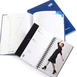 ANS Group Spółka z ograniczona odpowidzialnością - Otwarty kalendarz książkowy na spirali z datą 30 maja i zdjęciem kobiety, obok drugi otwarty kalendarz z datą 16 października, na tle granatowy kalendarz Pepco.