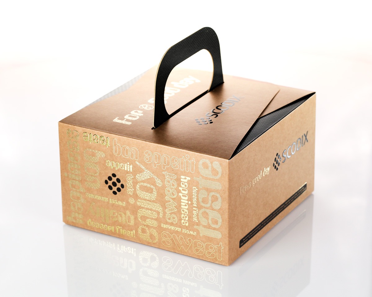 Brązowe, kartonowe opakowanie z uchwytem i złotymi napisami 'bon appetit', 'sweet' oraz logo Scodix na białym tle z odbiciem.
