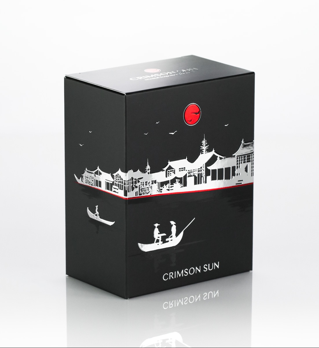 Czarne, prostokątne opakowanie z motywem orientalnym: srebrne budynki, łodzie i czerwone słońce. Napis 'Crimson Sun'.