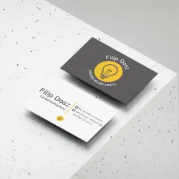 Dwie wizytówki na szarym, teksturowanym tle. Jedna biała z danymi kontaktowymi, druga grafitowa z logo firmy elektrycznej, żarówka w żółtym okręgu.