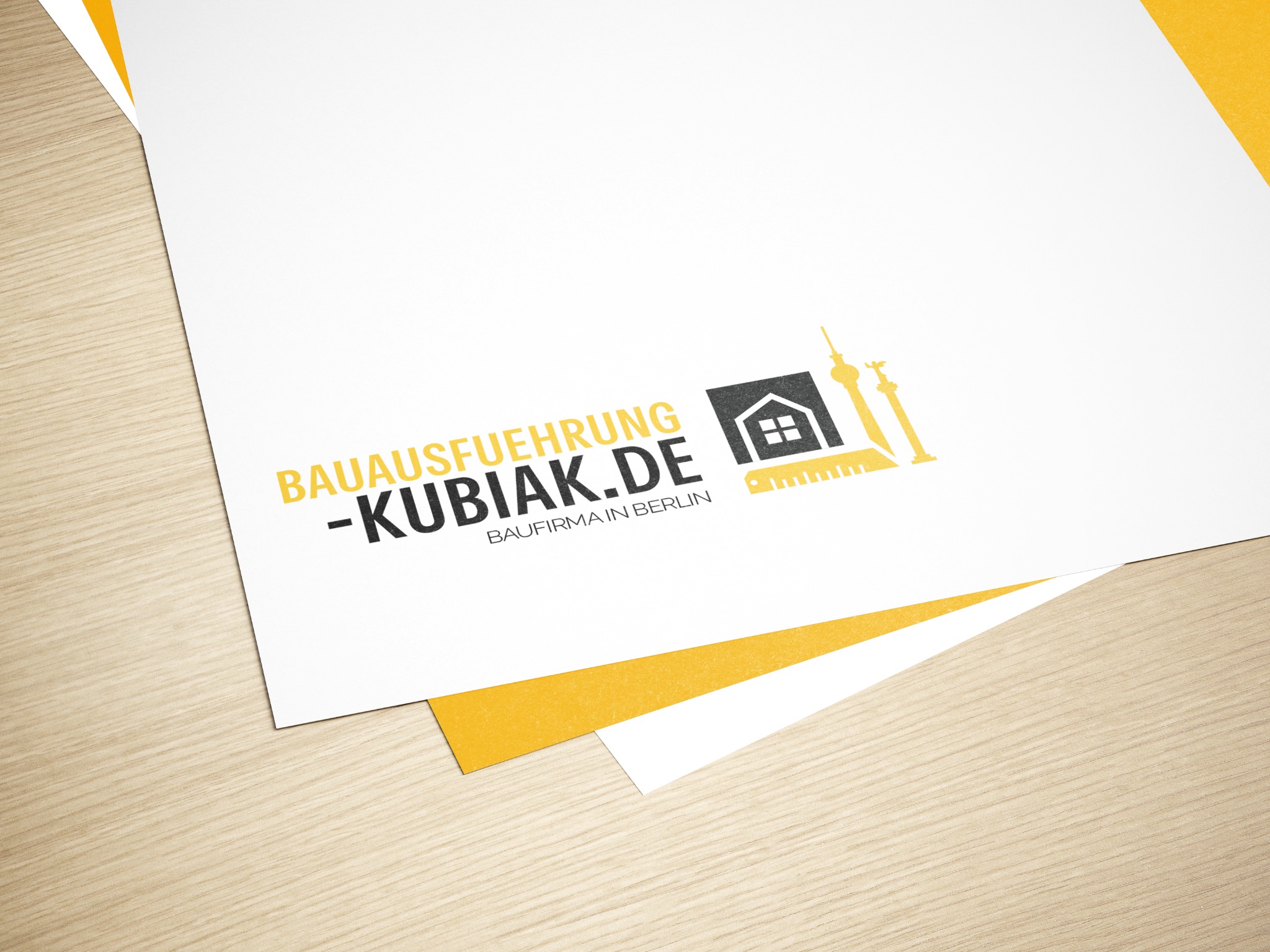 Stos kartek z nadrukowanym logo firmy budowlanej 'Bauausfuehrung-Kubiak.de' z motywem domu i wieży telewizyjnej na drewnianym tle.
