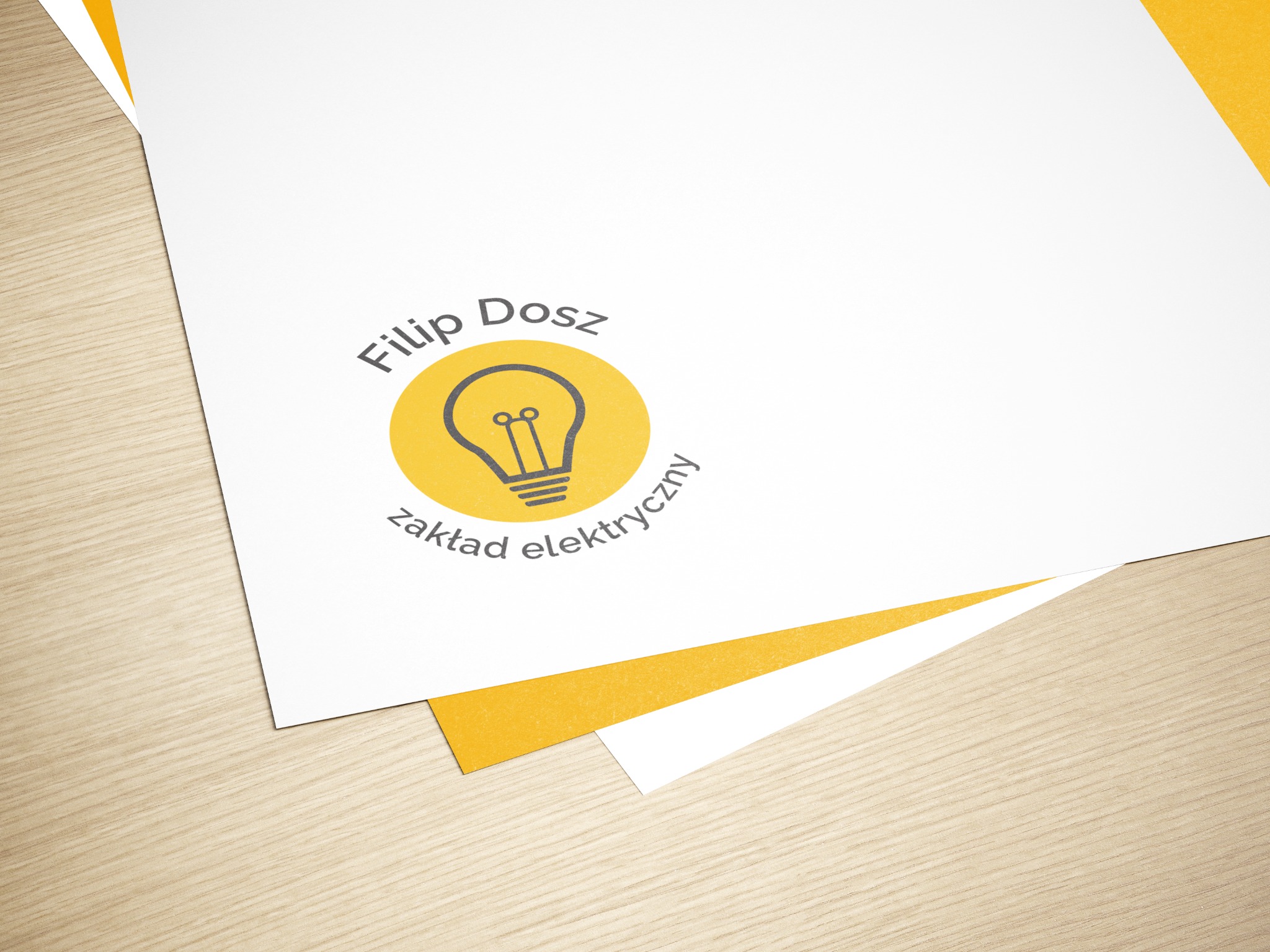 Wizytówka na białym papierze z logo firmy elektrycznej: żółta żarówka w okręgu i nazwa 'Filip Dosz zakład elektryczny' na drewnianym tle.