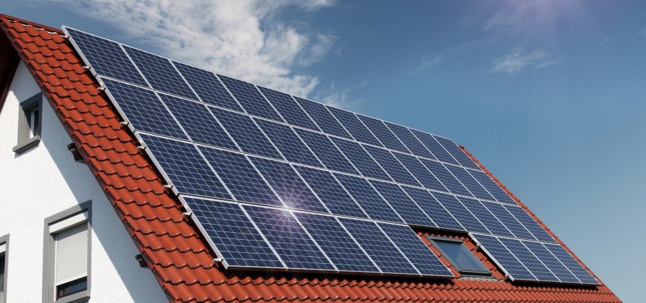 Panele słoneczne na czerwonym dachu domu jednorodzinnego z oknem dachowym, błękitne niebo w tle.