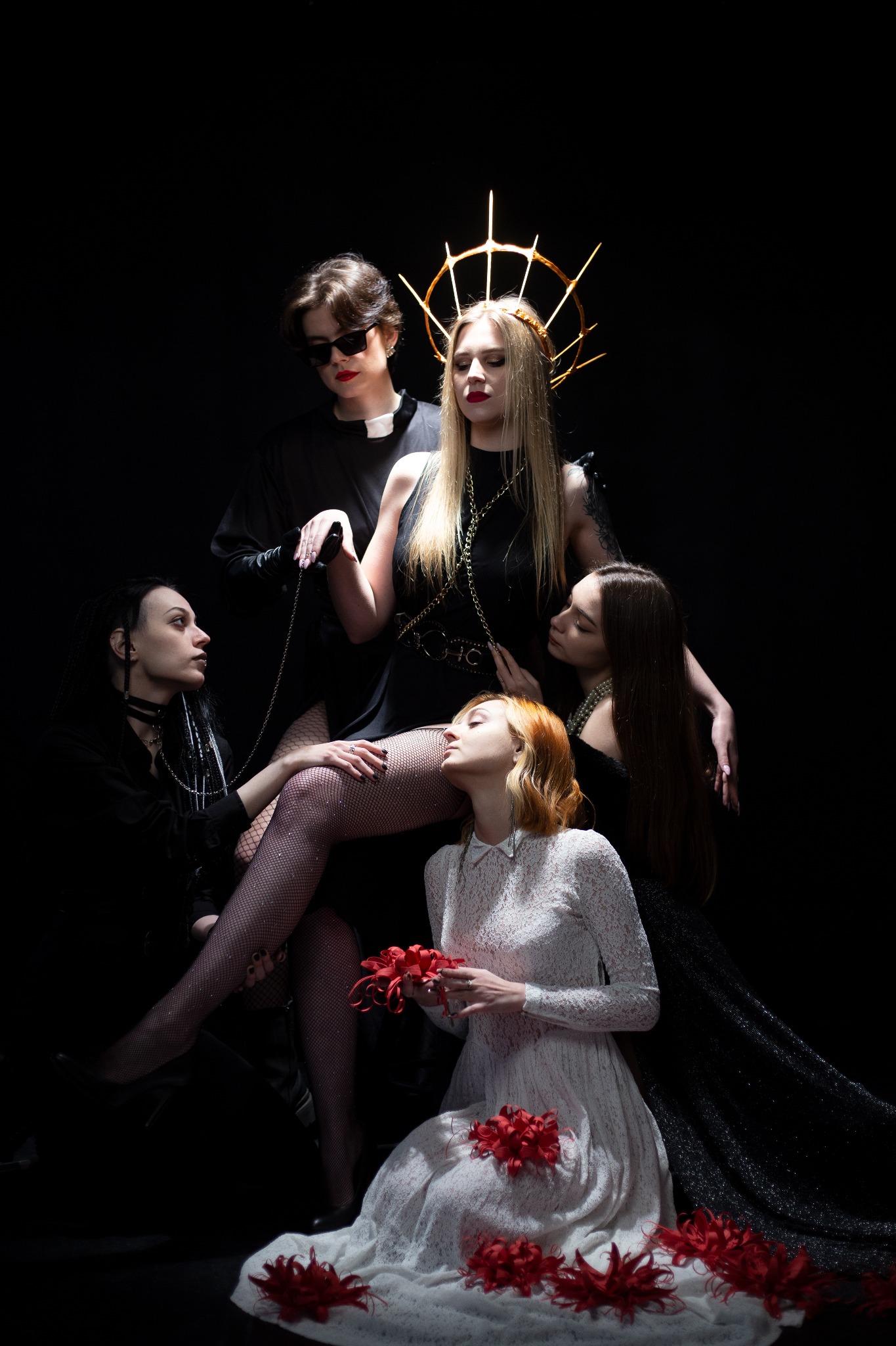 Stylizowana sesja z pięcioma modelkami w gotyckich i religijnych stylizacjach na czarnym tle, obejmująca kobietę w koronie, kobietę w sutannie i kobietę w białej sukni z czerwonymi kwiatami.