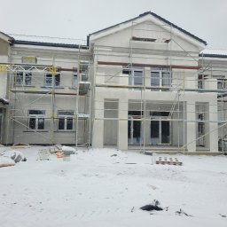 DYSTRYBUCJA 88 Sp. z o.o. - Budynek w trakcie ocieplania elewacji, pokryty rusztowaniami, z widocznym ośnieżonym terenem i padającym śniegiem.