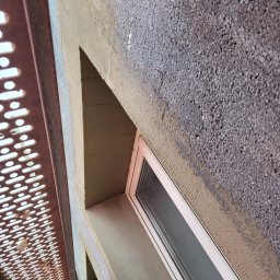 DYSTRYBUCJA 88 Sp. z o.o. - Fragment elewacji z oknem w trakcie tynkowania, widoczne rusztowanie i surowa powierzchnia obok gładkiego tynku.