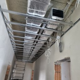 DYSTRYBUCJA 88 Sp. z o.o. - Sufit podwieszany z metalową konstrukcją, ocieplony wełną mineralną w folii aluminiowej, widoczne przewody elektryczne i drabina aluminiowa.
