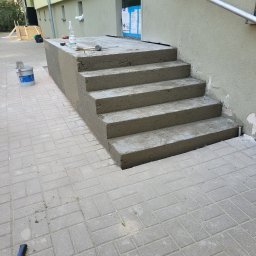 DYSTRYBUCJA 88 Sp. z o.o. - Świeżo wymurowane betonowe schody wejściowe do budynku, z widocznymi narzędziami murarskimi i butelką wody na górnym stopniu, na tle elewacji z zamontowaną balustradą.