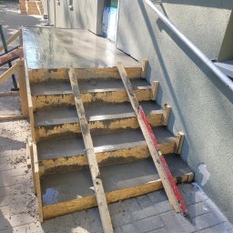 DYSTRYBUCJA 88 Sp. z o.o. - Betonowe schody w trakcie budowy, drewniane szalunki, poziomica oparta o ścianę budynku z elewacją.