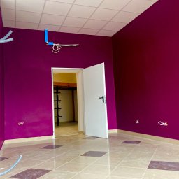 Arton - Pokój po malowaniu ścian na intensywny fioletowy kolor, widoczne elementy instalacji elektrycznej i wentylacyjnej przed zabudową, jasna podłoga z płytek w geometryczny wzór.