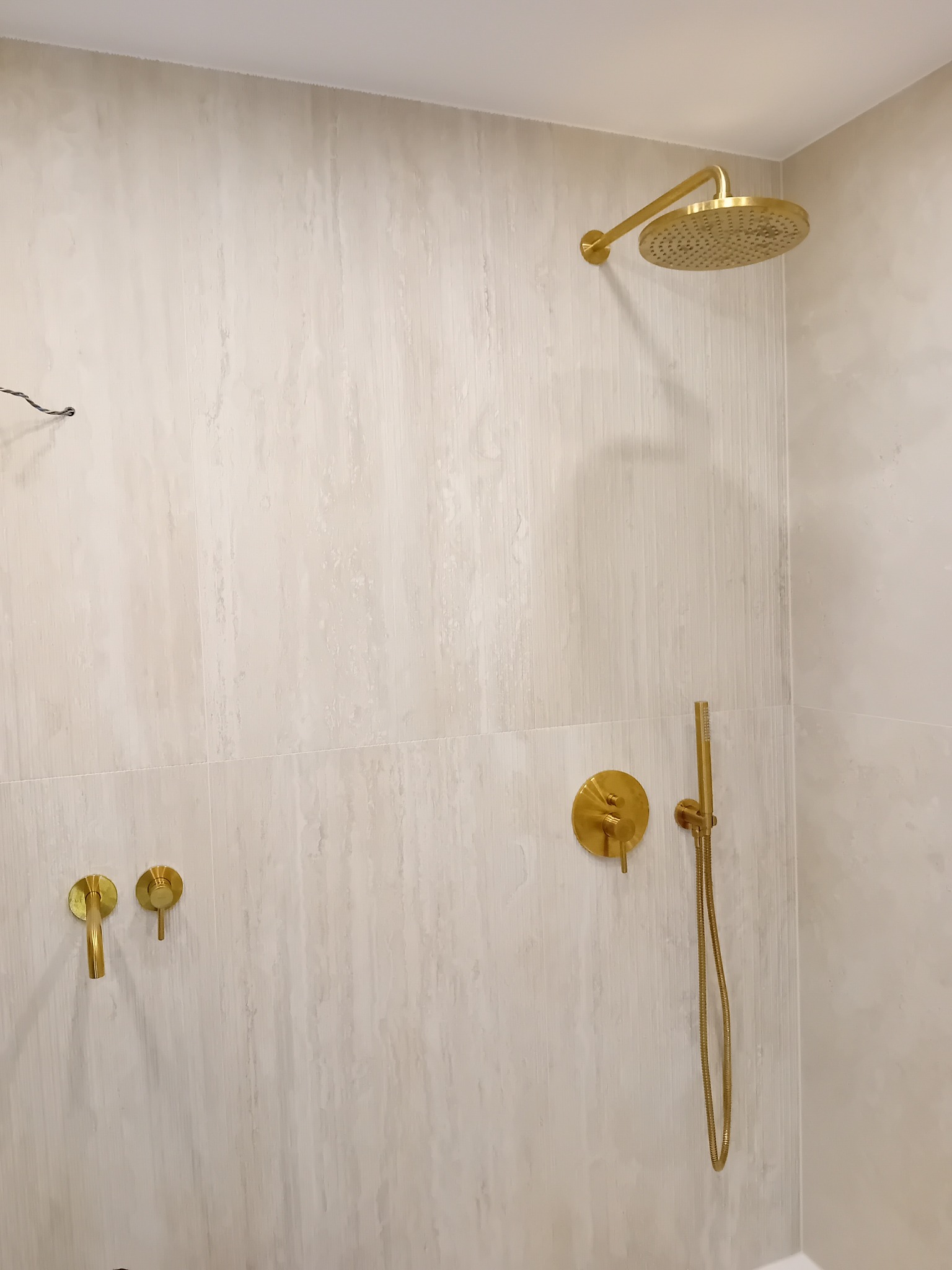 Nowoczesna kabina prysznicowa z armaturą w kolorze szczotkowanego złota, ściany wykończone płytkami imitującymi trawertyn.