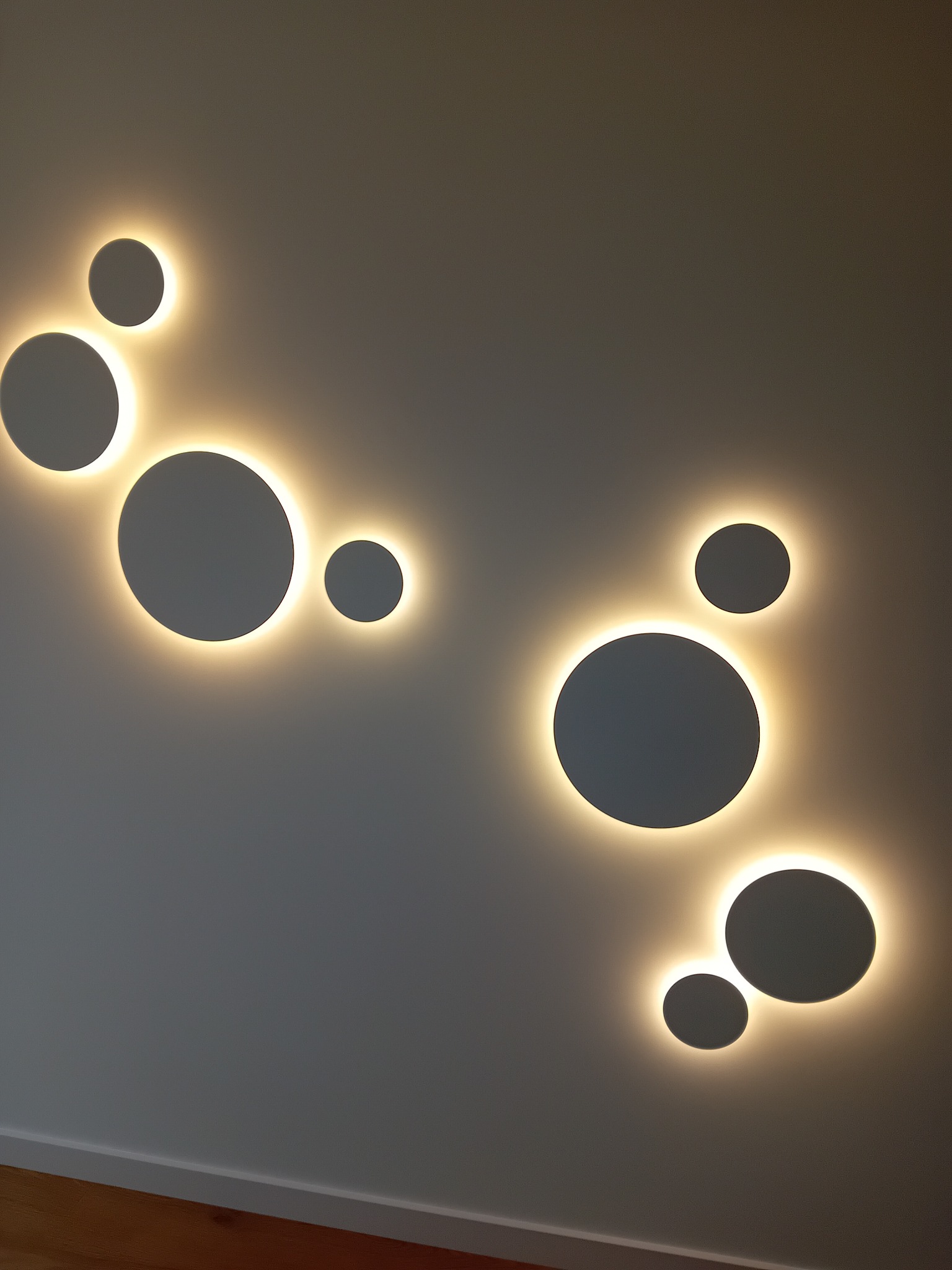 Dekoracyjne oświetlenie ścienne w kształcie okręgów z podświetleniem LED w Markach, tworzące nowoczesny wzór na szarej ścianie.