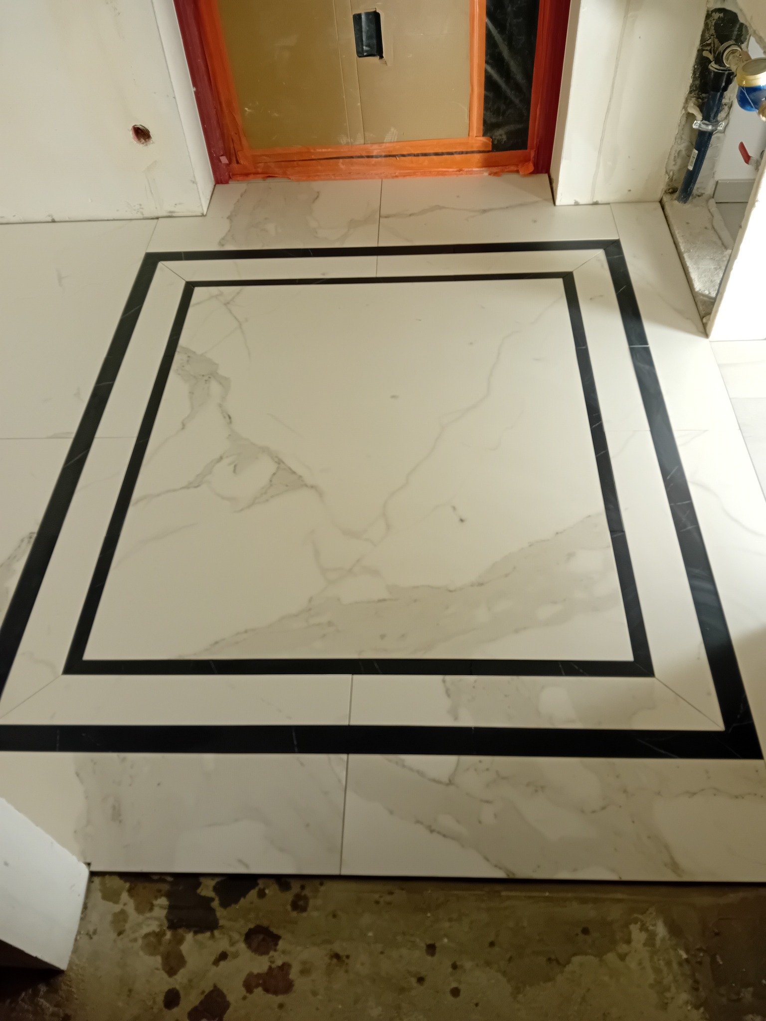 Wykończona podłoga z białych płytek imitujących marmur, z czarną bordiurą, widoczne niedociągnięcia przy ścianach i brudne podłoże.