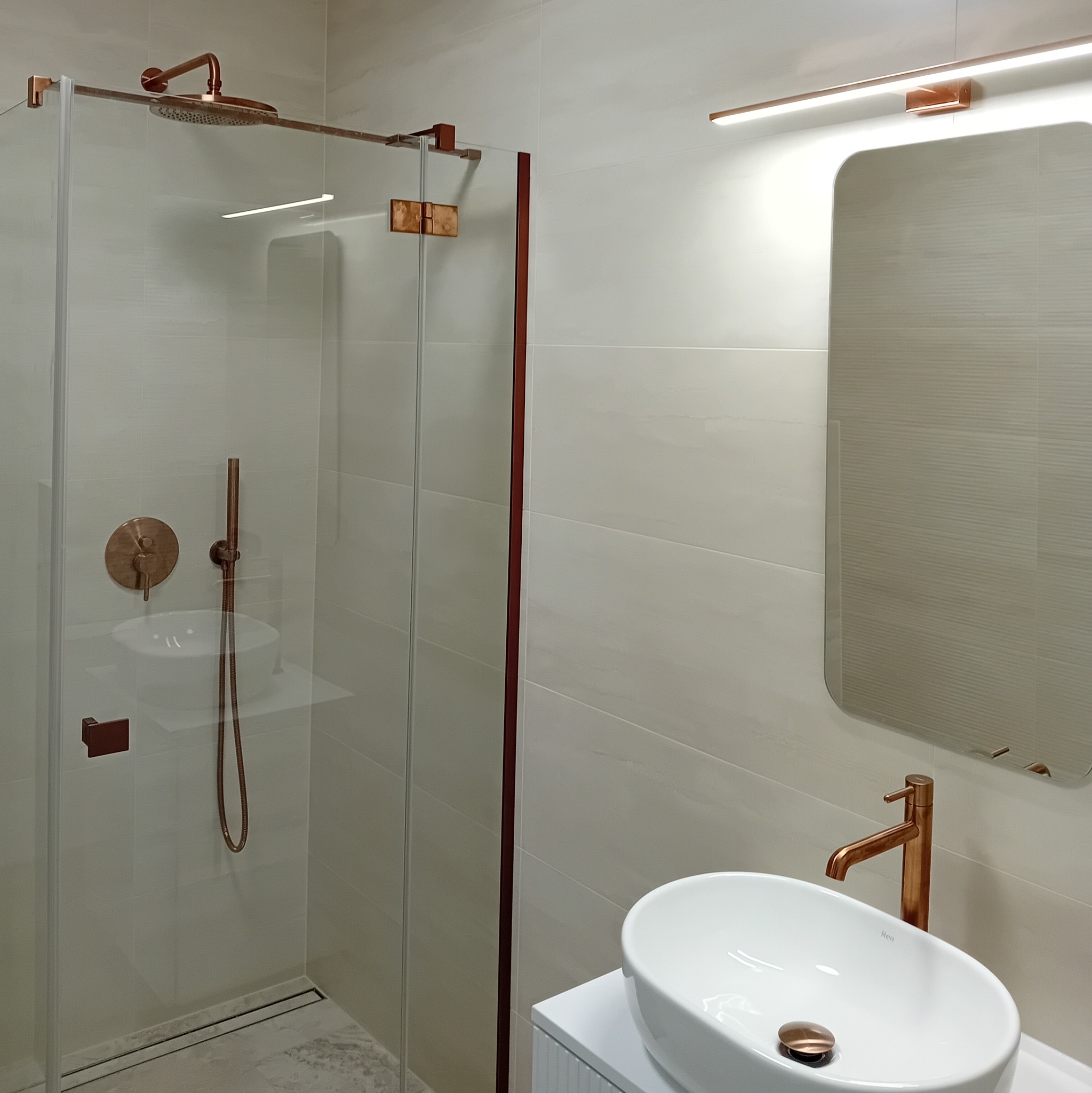 Nowoczesna łazienka z kabiną prysznicową typu walk-in, armaturą w kolorze miedzi i owalną umywalką nablatową.