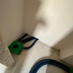 Zielona skrzynka rozdzielcza z podłączonymi karbowanymi rurami wentylacyjnymi, widok w rogu pomieszczenia w stanie surowym.