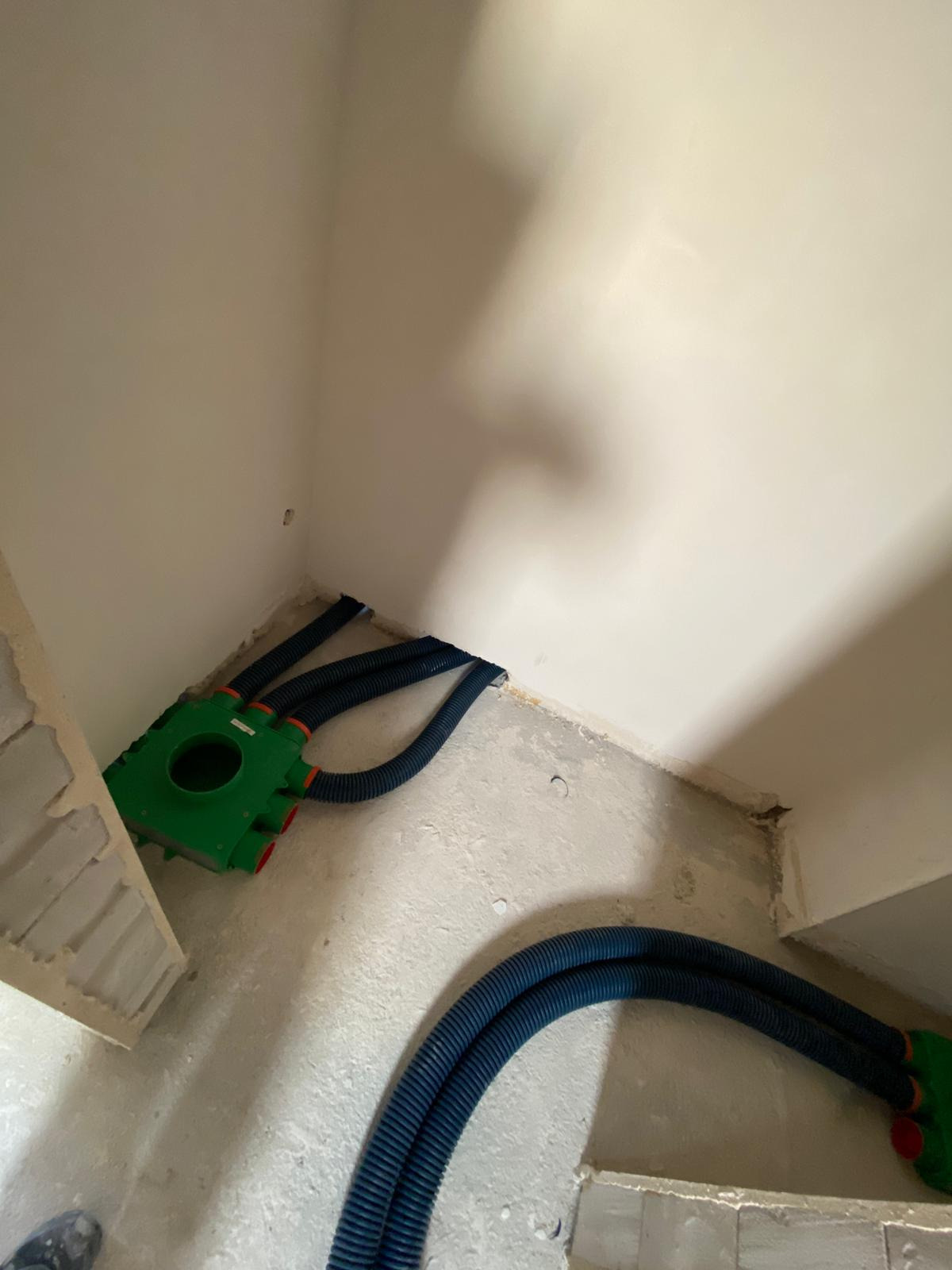 Zielona skrzynka rozdzielcza z podłączonymi karbowanymi rurami wentylacyjnymi, widok w rogu pomieszczenia w stanie surowym.