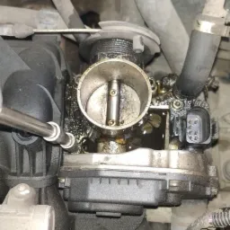 Czyszczenie przepustnicy w samochodzie, widoczne ślady oleju i narzędzie.