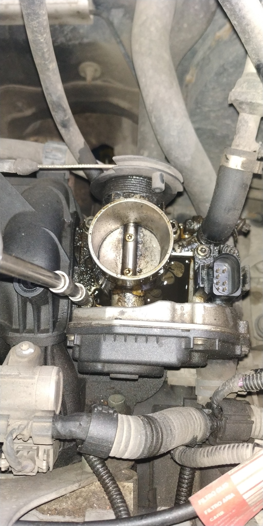 Czyszczenie przepustnicy w samochodzie, widoczne ślady oleju i narzędzie.