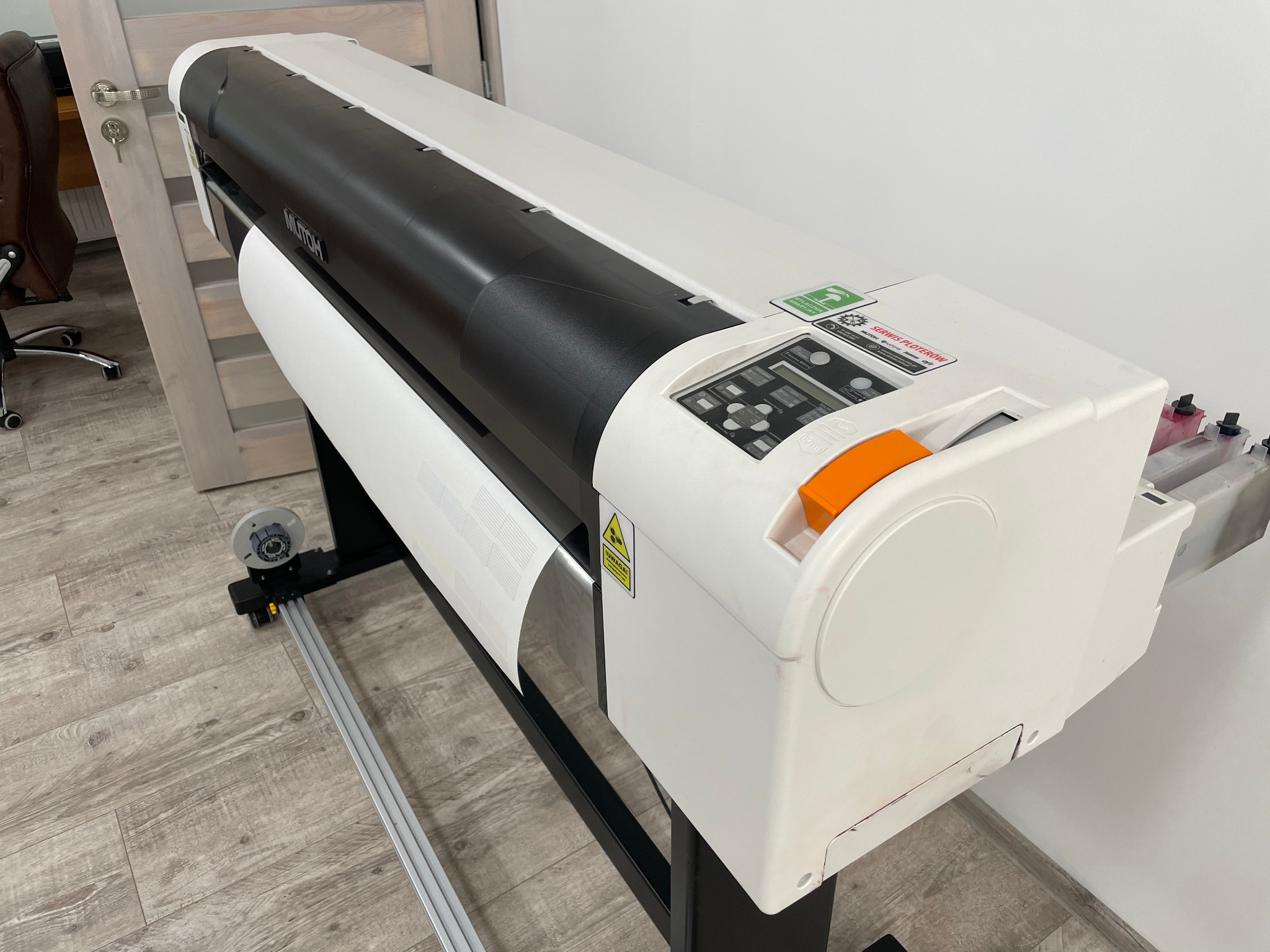 Szerokokątny widok plotera drukującego na białym papierze z widocznymi pojemnikami z tuszem.