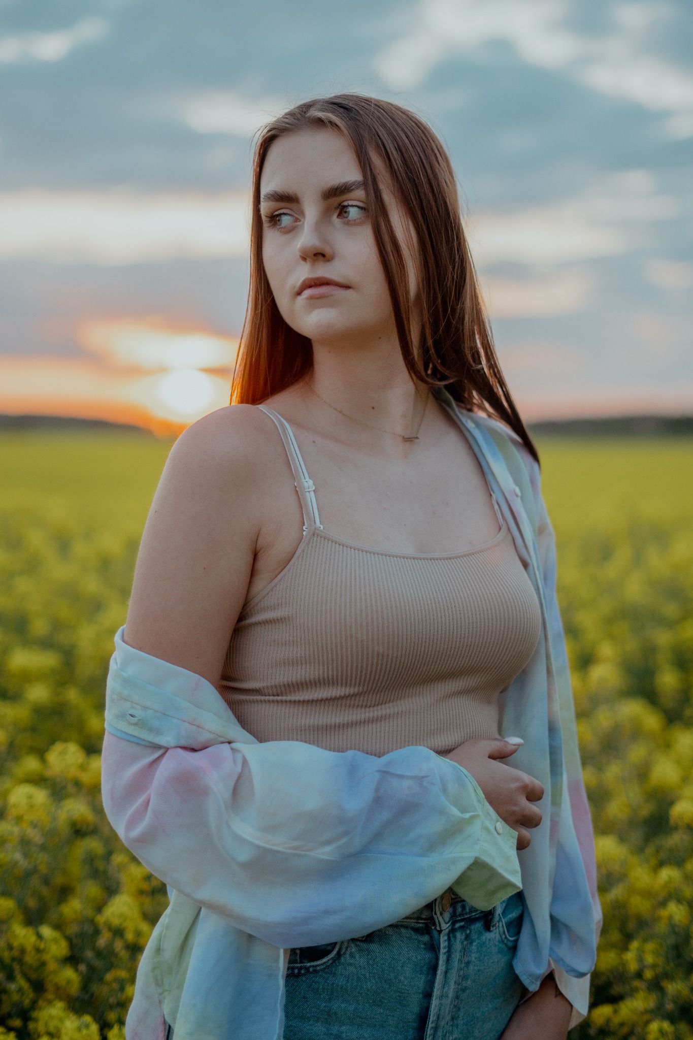 Portret Zuzanny Szcześniak na tle zachodzącego słońca i kwitnącego pola rzepaku, ubrana w beżowy top i jeansową koszulę.
