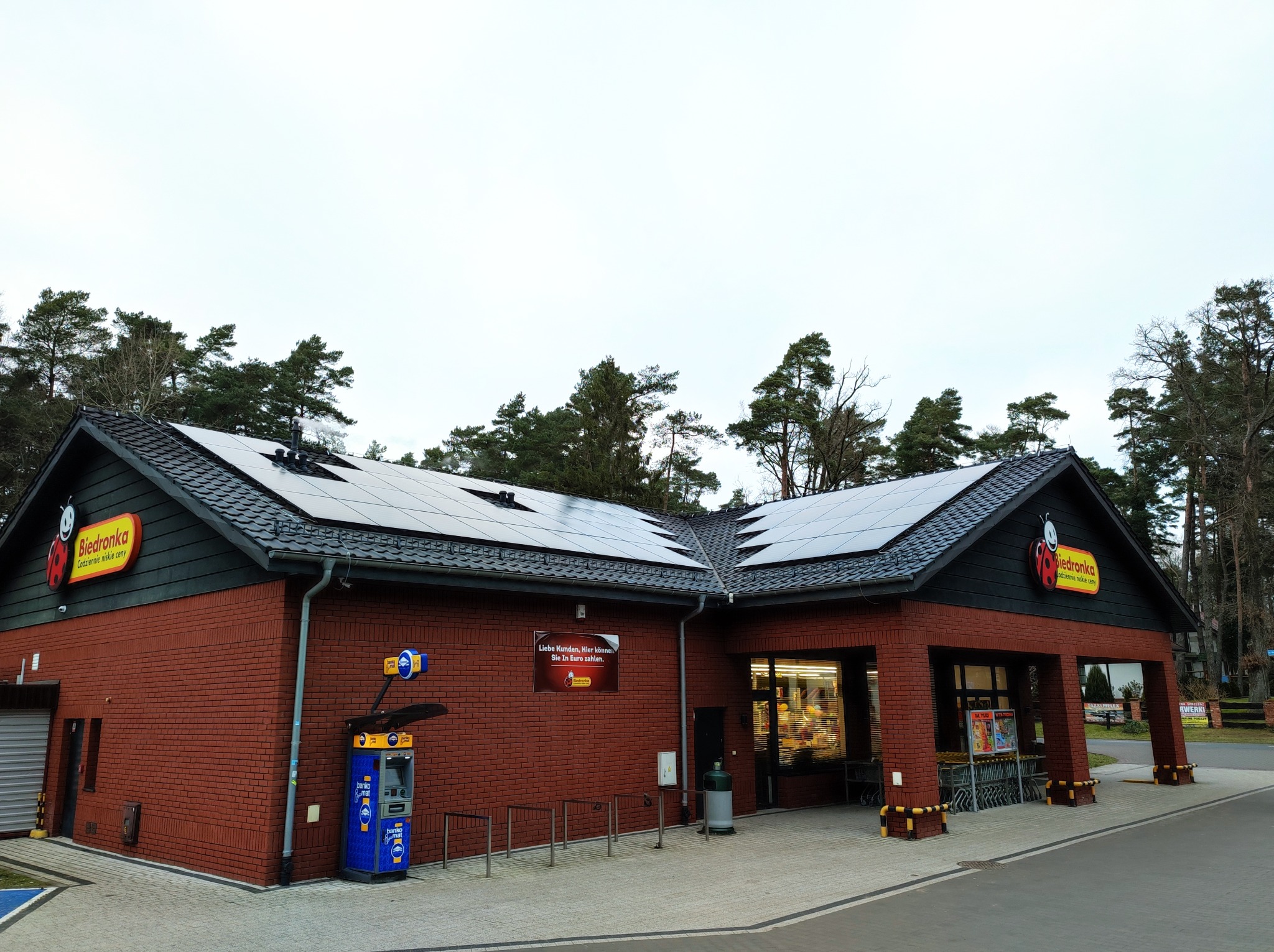 Budynek sklepu Biedronka z panelami słonecznymi na dachu, widok z zewnątrz w pochmurny dzień.