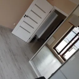 Jasne panele podłogowe w pokoju z białymi drzwiami z przeszkleniami i dużą szafą wnękową z przesuwnymi drzwiami.