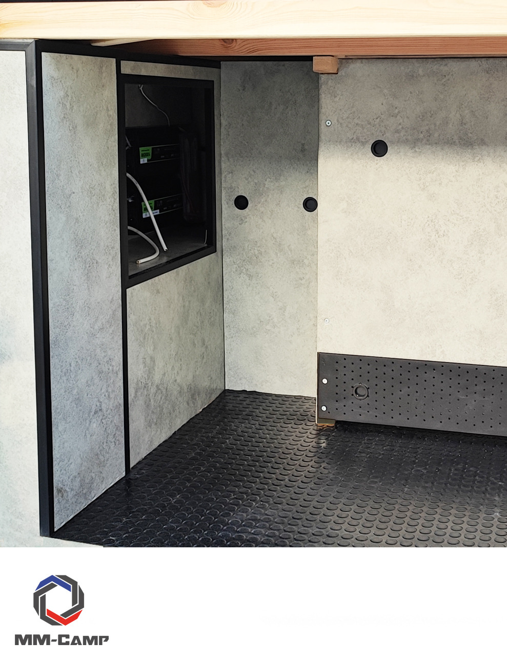 Wnętrze szafy z wnęką na urządzenia elektroniczne, wykończone panelami w odcieniach szarości i czarną podłogą z wypustkami, widoczne kable i elementy montażowe.