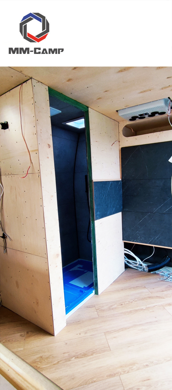 Wnętrze w trakcie wykańczania: drewniana konstrukcja kabiny prysznicowej z niebieskim brodzikiem, częściowo wykończona ściana z płytkami imitującymi marmur, widoczne przewody i instalacje.