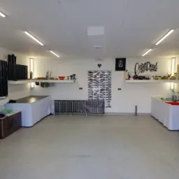 Przestronne, dobrze oświetlone studio z przygotowanym stanowiskiem pracy, rolkami folii i narzędziami na półkach, plakatami i listą modeli samochodów na ścianach, gotowe do pracy nad pojazdami.