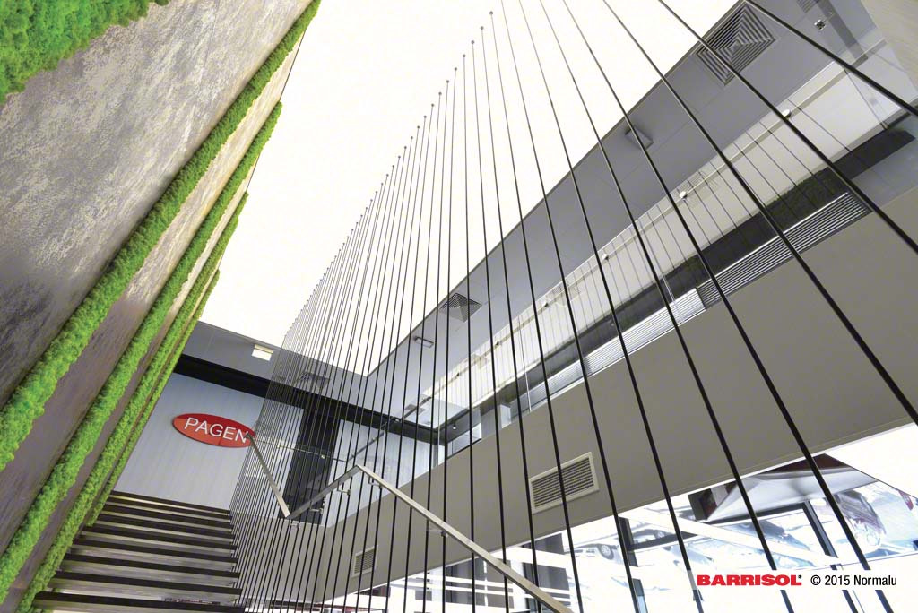 Wnętrze biura z zieloną ścianą z mchu, logo firmy PAGEN, schodami i szklaną balustradą z pionowymi czarnymi prętami.