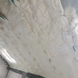 Poddasze ocieplone jasną pianką, widoczne elementy konstrukcyjne i mocowania.