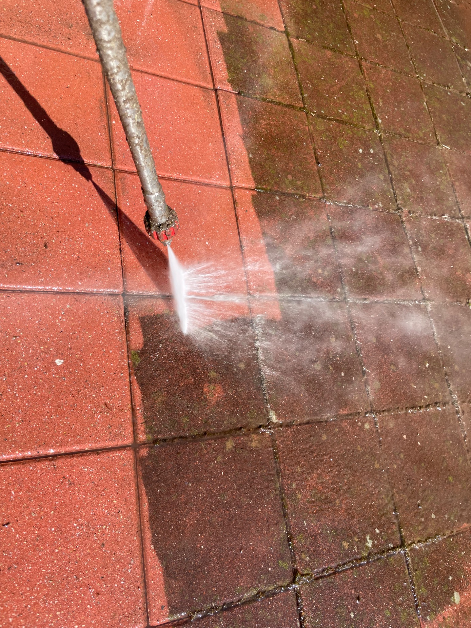 Czerwona kostka brukowa czyszczona strumieniem wody pod ciśnieniem, widoczna różnica między czystą a zabrudzoną powierzchnią.