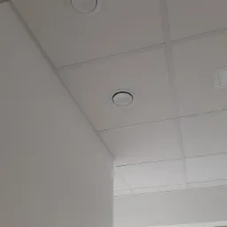 Sufit podwieszany z dwoma okrągłymi nawiewnikami w pomieszczeniu biurowym, widok z dołu, minimalizm wnętrza.