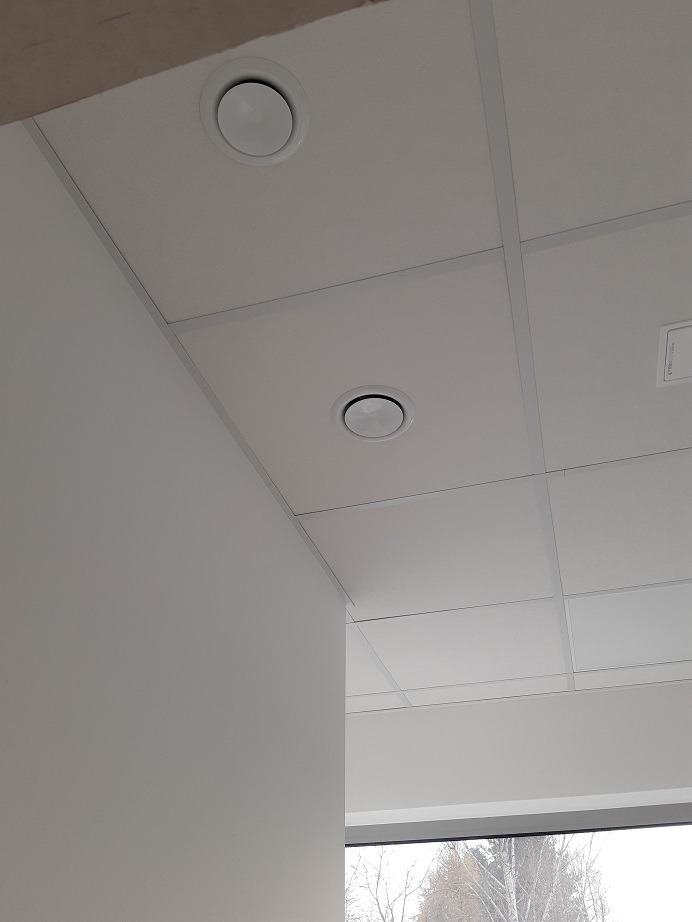 Sufit podwieszany z dwoma okrągłymi nawiewnikami w pomieszczeniu biurowym, widok z dołu, minimalizm wnętrza.