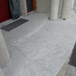 Wykończony taras przed budynkiem z jasnoszarej płyty z wyraźnym wzorem żyłkowania, widoczne kolumny i kratka ściekowa przy drzwiach.