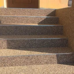 Schody wejściowe wykończone żywicą epoksydową z drobnym kruszywem, z metalowymi listwami zabezpieczającymi krawędzie stopni.