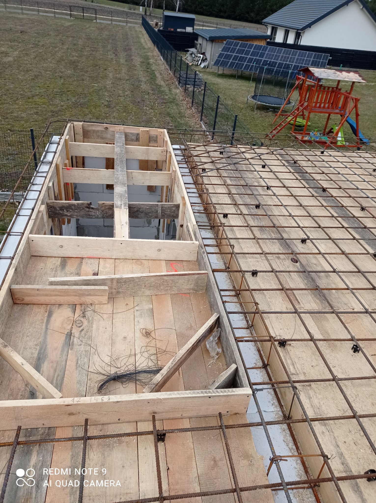 Szalunek z desek i zbrojenie z prętów stalowych na budowie domu jednorodzinnego, widok z góry na przygotowaną konstrukcję stropu z widocznymi elementami mocującymi i fragmentem izolacji obwodowej.