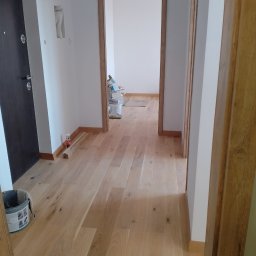 Stefan Olszynka - Jasne panele podłogowe ułożone w korytarzu z widocznymi listwami przypodłogowymi i ościeżnicami. W tle wiadro i materiały budowlane.