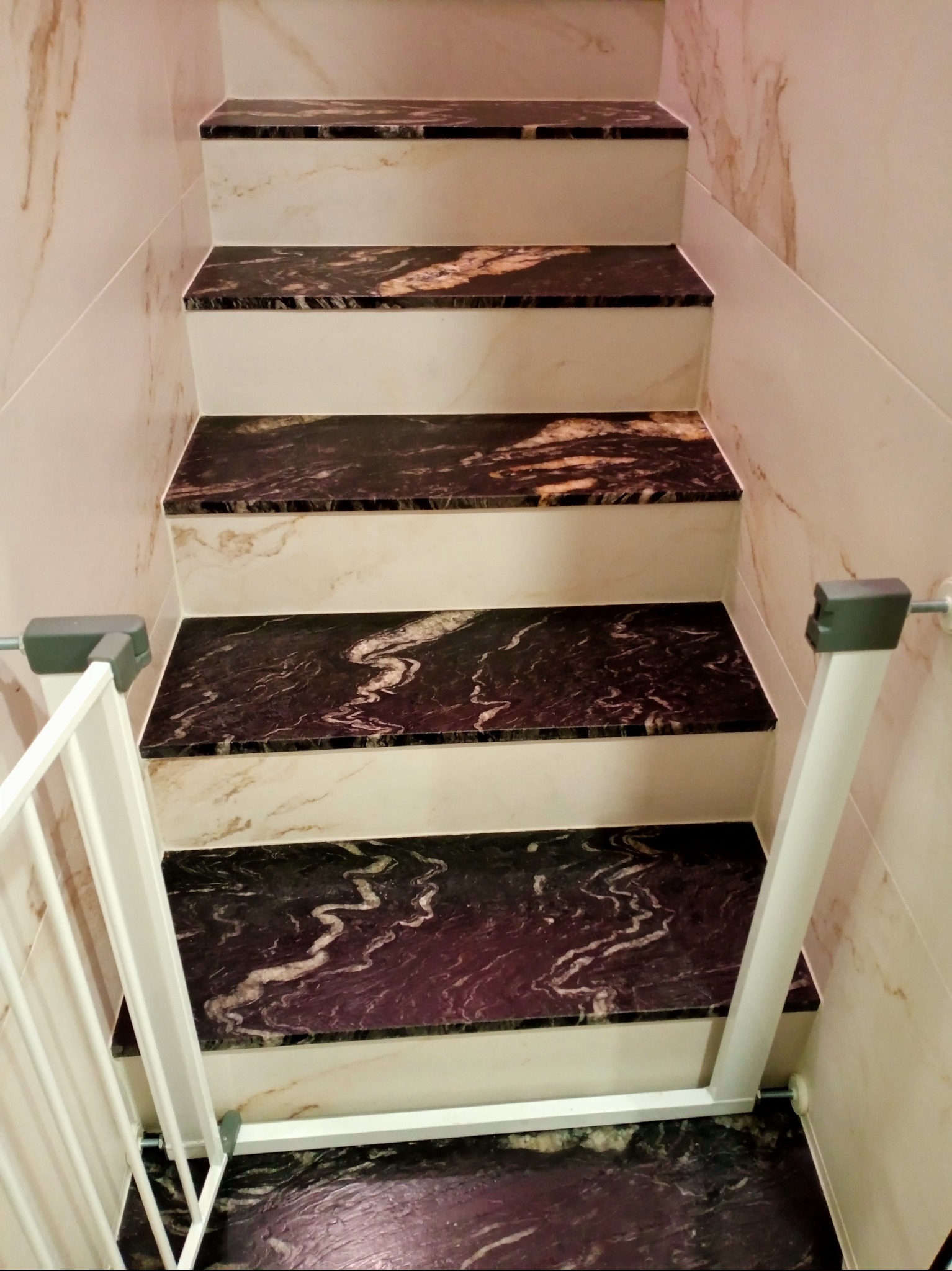 Schody wyłożone płytkami imitującymi marmur, zabezpieczone białą barierką. Widok z góry ukazuje wzór płytek i estetyczne wykończenie.