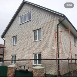 Dwukondygnacyjny dom z jasnej cegły z białymi ramami okiennymi, widoczne rusztowanie i numer domu '17'.