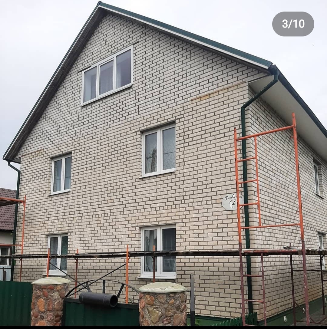 Dwukondygnacyjny dom z jasnej cegły z białymi ramami okiennymi, widoczne rusztowanie i numer domu '17'.